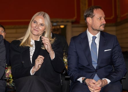 Norway’s crown princess Mette-Marit sits next to crown prince Haakon at the 100th anniversary of the library in Fredrikstad, Norway. She is wearing a black jacket, he is wearing a blue suit with a blue tie.