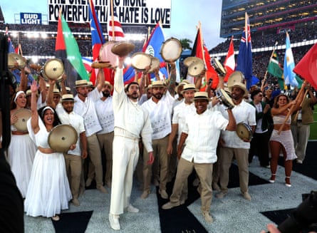 A man holds up a football while he’s surrounded by a band and people holding up various nation’s flags