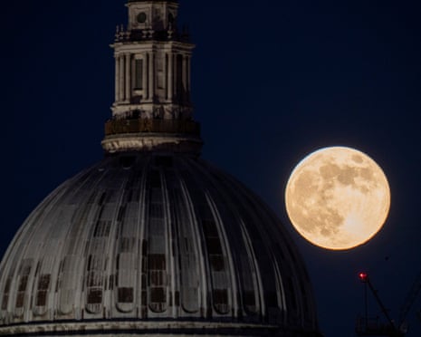 A full moon appears beside the illuminated dome of St Paul's Cathedral against a dark blue sky