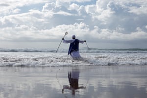 A man dressed in religious gowns stands in waves from the ocean
