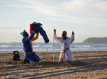 Image 19: Two men in robes pray on a beach