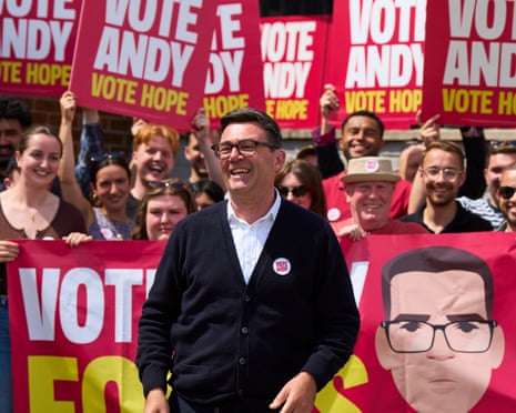 Andy Burnham smiling outdoors, backed by supporters holding banners and placards that say Vote Andy, Vote Hope and Vote Andy for us