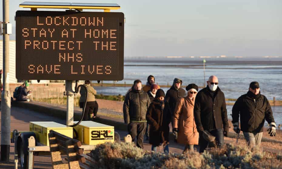 People walk past a digital public safety notice saying “Lockdown, Stay at Home, Protect the NHS, Save Lives” along the seafront at Westcliff beach in Southend on 9 January 2021