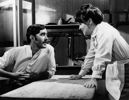 Pauline Collins in white blouse leaning on a table opposite John Alderton, who’s staring at her