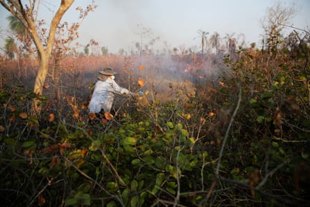 A person with their face covered in an area of dry brush as smoke rises