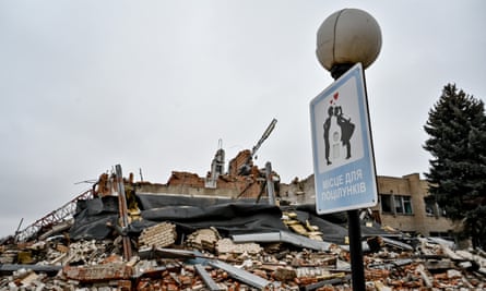 A lamppost and a sign reading in Ukrainian “‘A place to kiss’ near a building destroyed in the shelling of Huliaipole