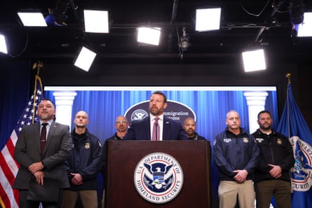 a man speaking on a podium with six men standing behind him