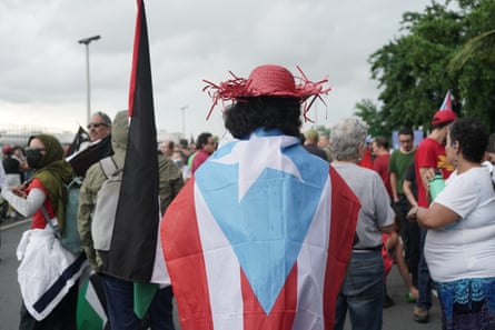 A man wearing a red straw hat with a flag on his back, with red and white lines, with a light blue triangle and a white star.