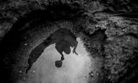 Eudicia, 12, is reflected in a hand-dug water hole in the dry riverbed of the river Lurio near Muassi village, in the province of Niassa, Mozambique.