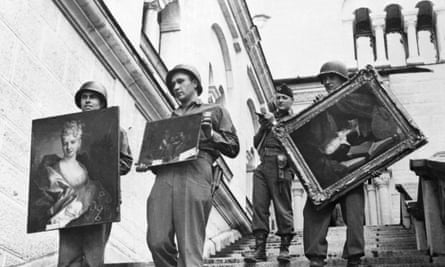 Photograph of three US soldiers walking down a flight of stairs holding up paintings to the camera while an officer further up the staircase holds a list
