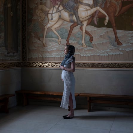 Yulia Кара standing in profile in front of a mural featuring horses