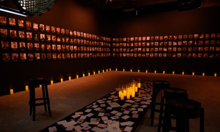 A room lit with dim light and candles in the centre of the floor, with softly lit photographs of people around the walls