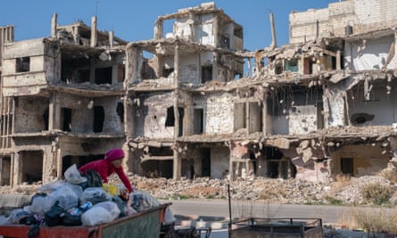A boy sifts through trash to find recycling to sell in Homs, Syria. Behind are the shells of destroyed buildings