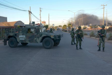 Soldiers stand guard near burning vehicles on a street during the operation to arrest Guzmán