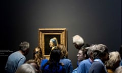 people gather around vermeer's girl with a pearl earring, alone and spotlit on a charcoal grey wall at the Rijksmuseum in Amsterdam, February 2023.