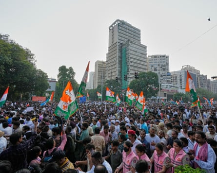 A large crowd of people, some holding flags, walk through Delhi