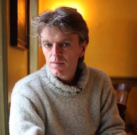 A man in a roll-neck sweater with short blond hair staring at the camera