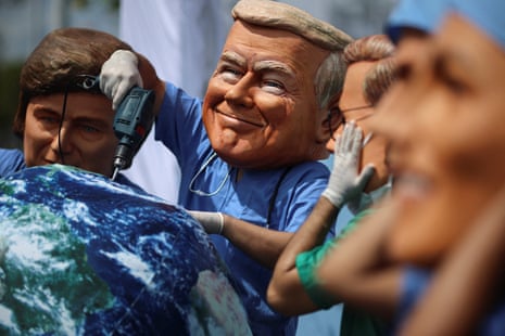 people wear oversized masks depicting world leaders, including one holding a power drill over a ball representing the earth