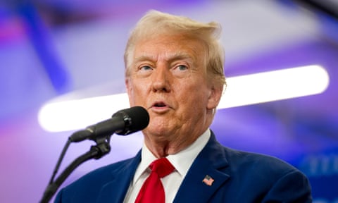 Donald Trump in red tie and suit speaks into microphone