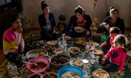 Women and children sit on a carpet to share a meal.