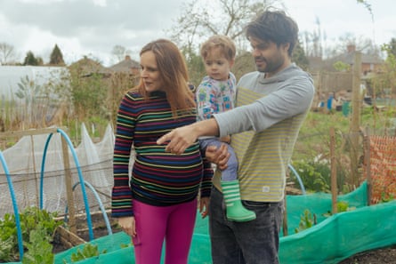Helen Tim and Raphael on their allotment. Tim is holding Raphael and pointing