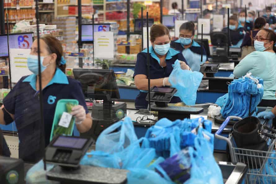 Diana Rivero stands behind a partial protective plastic screen and wears a mask and gloves as she works as a cashier at the Presidente Supermarket on April 13, 2020 in Miami, Florida. The employees at Presidente Supermarket, like the rest of America’s grocery store workers, are on the front lines of the coronavirus pandemic, helping to keep the nation’s residents fed.