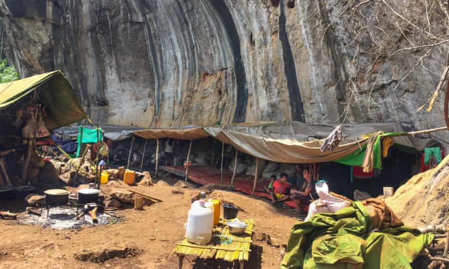 People sheltering under tarpaulins against a cliff face