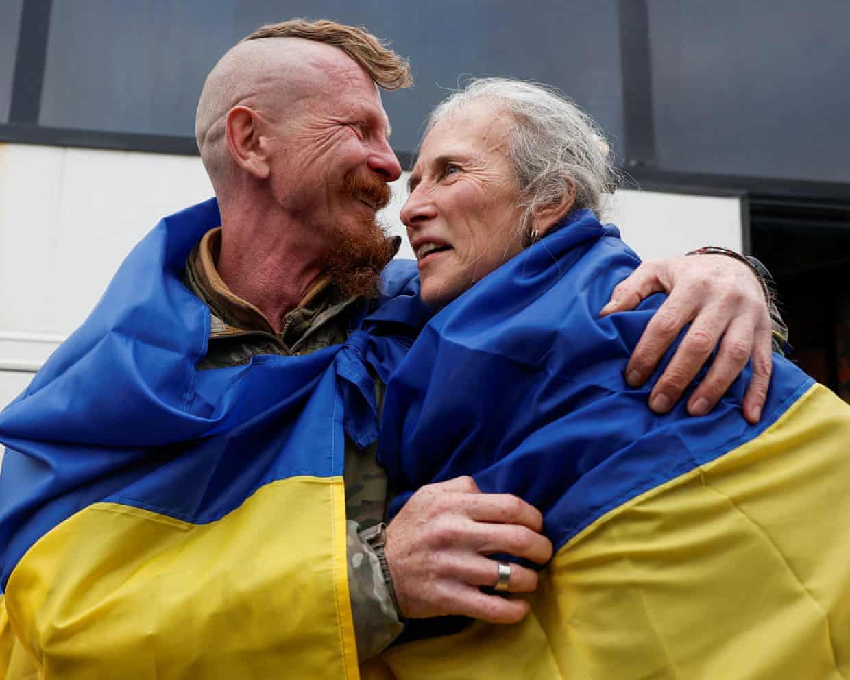 Dmytro and Larysa, evacuated residents, embrace wrapped in a Ukrainian flag