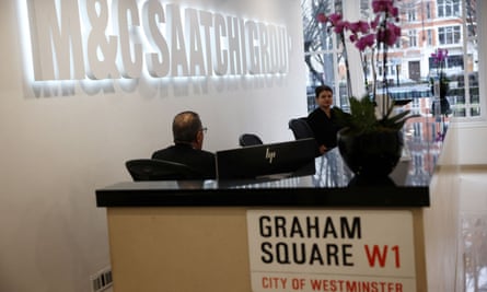 Man and woman sit on reception desk, to which is attached a street sign that reads Graham Square W1