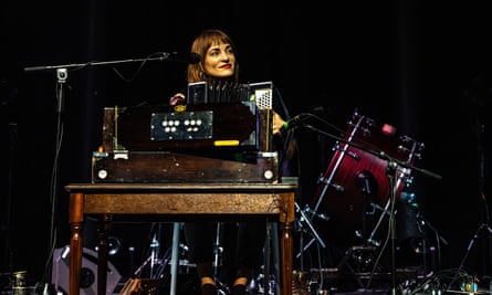 Radie Peat smiling, largely obscured by a bankd of harmoniums and accordion