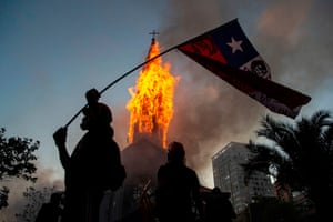 A demonstrator flies a Chilean flag outside the burning church of Asuncion, set on fire by protesters in Santiago, Chile