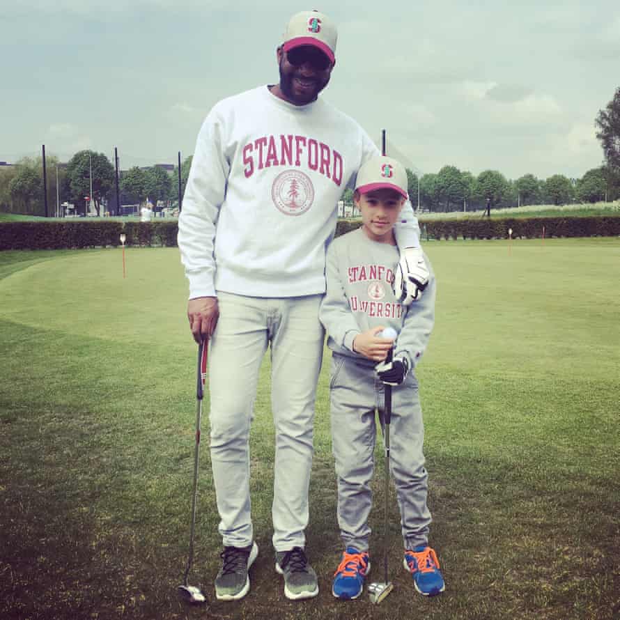 An adult and child holding golf clubs, dressed in Stanford sweatshirts and caps