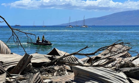People on a jet ski cruise by destroyed buildings and homes in the aftermath of a wildfire in Lahaina, western Maui, Hawaii on August 11, 2023.