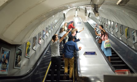 Groups of passengers cheer and sing about the night tube on the Oxford Circus escalators. Alex and Ibbi are on the right.
