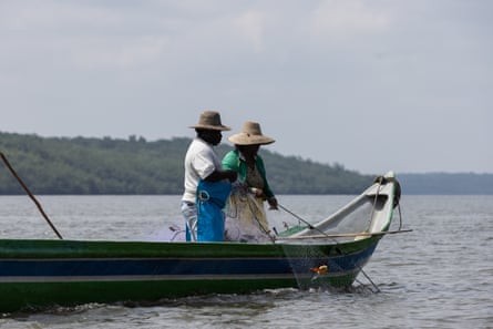 Two fishermen stand in the prow of a small boat with nets