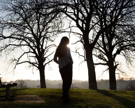 A silhouetted figure stands between bare trees on a hilltop at sunset