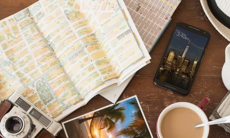 Array of a travel-related items grouped on a table, including a smartphone, map, camera and a mug of tea.