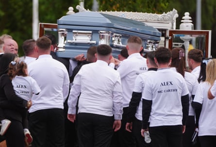People carry a light blue coffin while wearing white T-shirts with Alex McCarthy's name on them