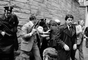 Secret service agents and police officers swarm a gunman, hidden from view, after he attempted an assassination on President Ronald Reagan on 30 March 1981.