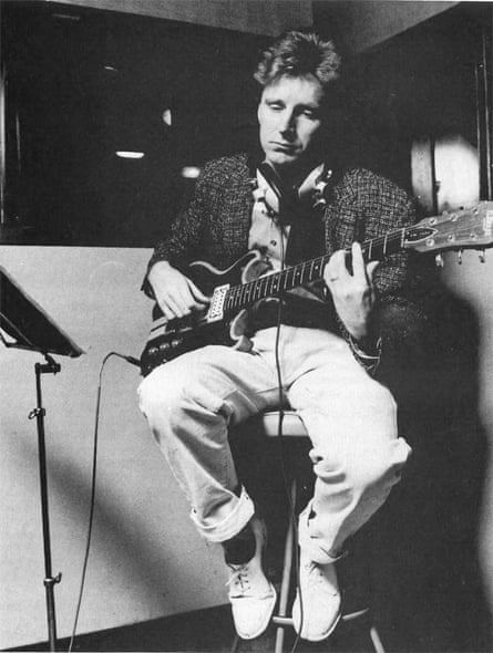 A picture of Robin Millar as a young man sitting in a chair playing the guitar