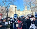 A crowd of people in winter clothing gather with protest signs outside City Hall.