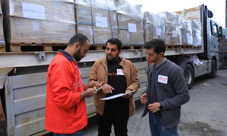 Three men stand together in front of a lorry loaded with large cardboard boxes on pallets.