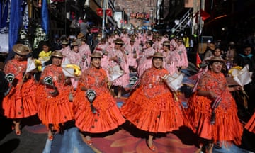 Women in orange and pink dresses dance in a parade along a street in La Paz