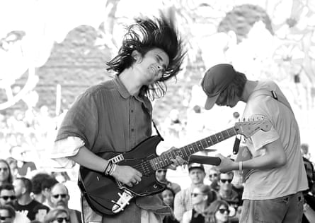 A black and white image of a man in a denim shirt shaking his head and playing his guitar