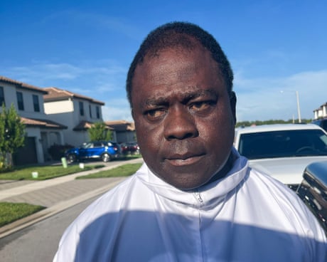 man in a white jacket looksto the side on a residential street by cars