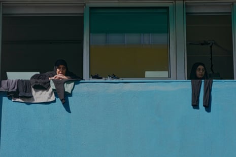Two women in dark hijabs sit looking out of two windows that are side by side.