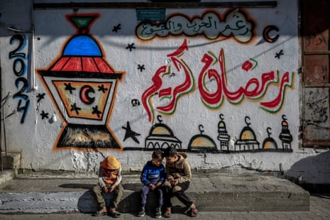 Palestinian children sit in front of a wall bearing Ramadan theme drawings in Gaza City on Friday.