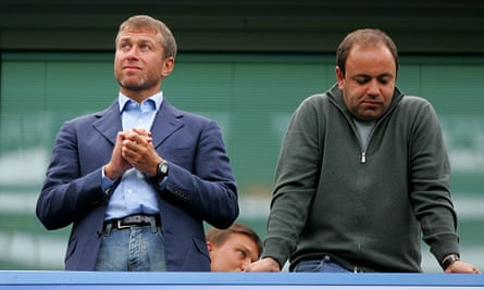 Roman Abramovich stands with his hands clasped looking at something off camera while next to him Shvidler leans on a railing looking downwards