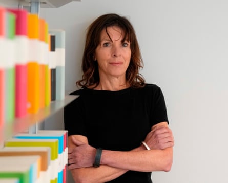 Writer Rachel Cusk stands with arms crossed beside a shelf of colourful books