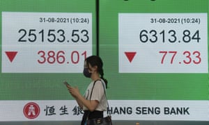 A woman wearing a face mask walks past a bank’s electronic board showing the Hong Kong share index.